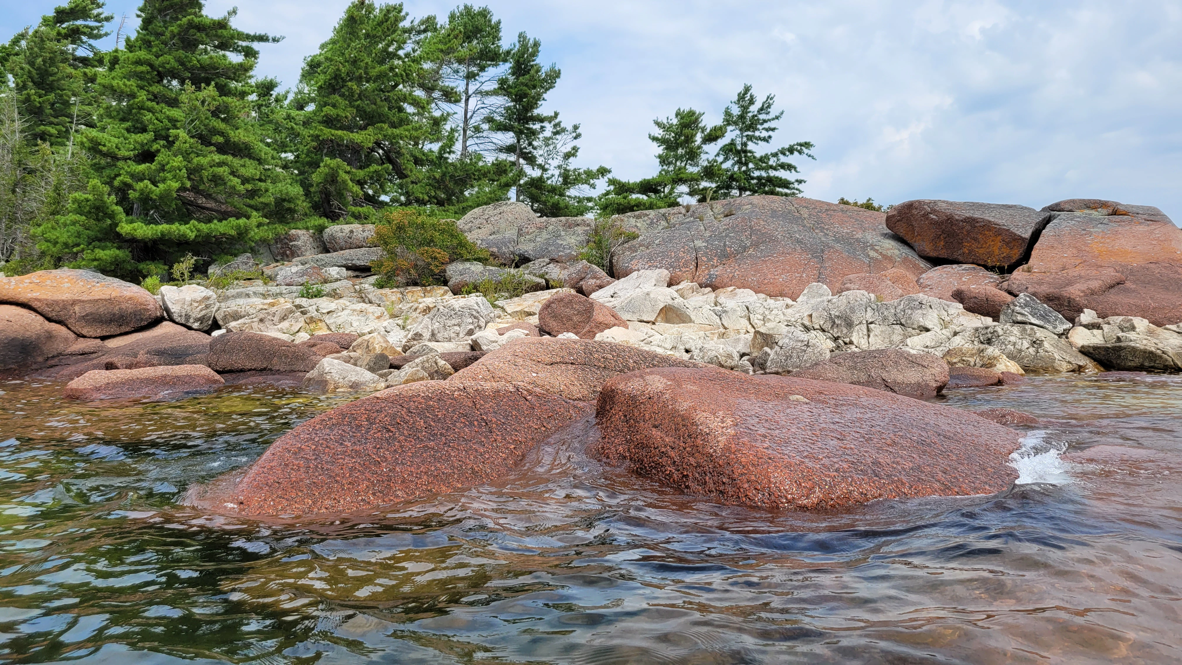 Western Shoreline of the Benjamind islands with red granite rock, white quartzite,
                trees and clear water